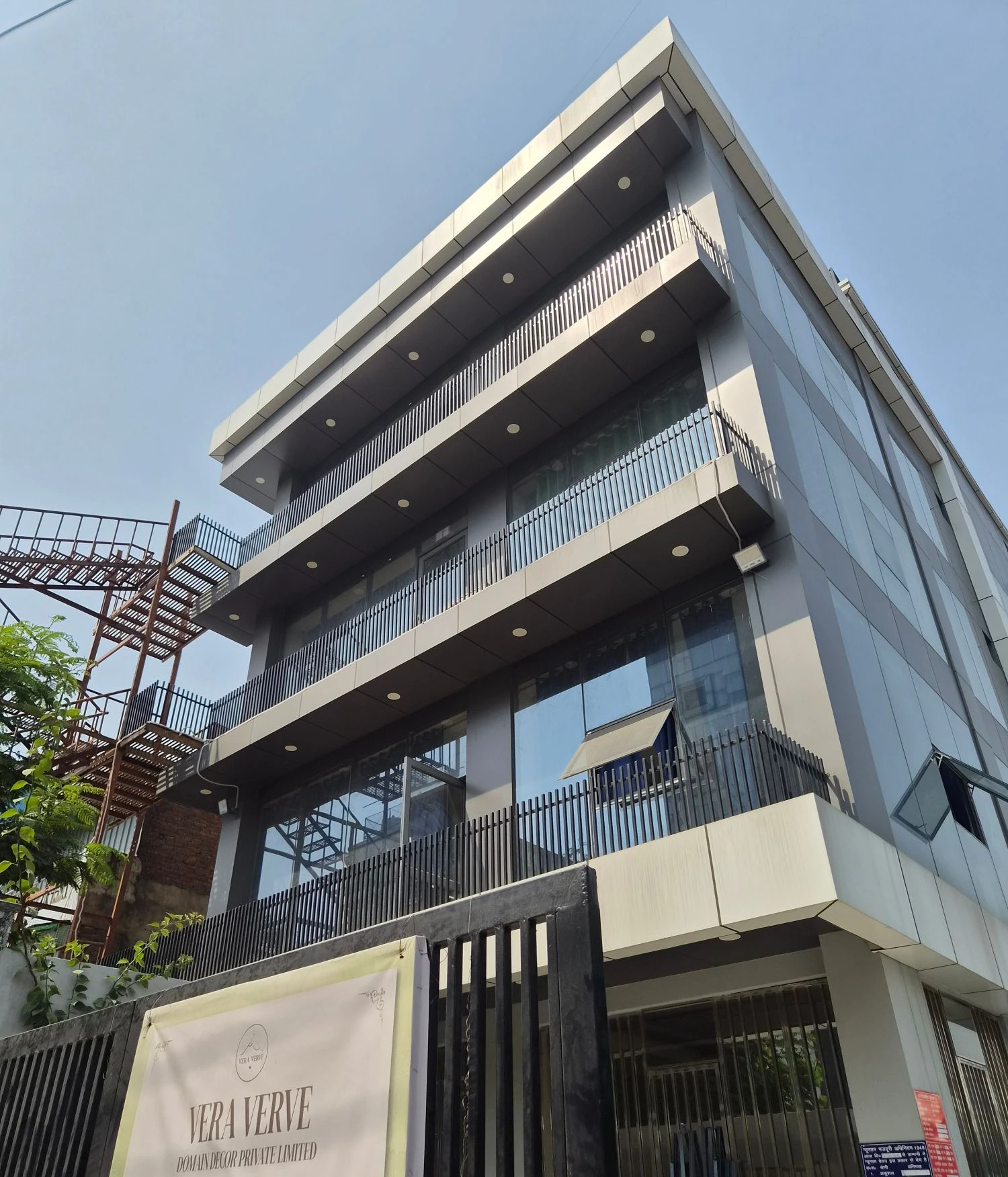 The Vera Verve building in Noida: a grey building with long balconies, seen from the front gate with the Vera Verve sign.
