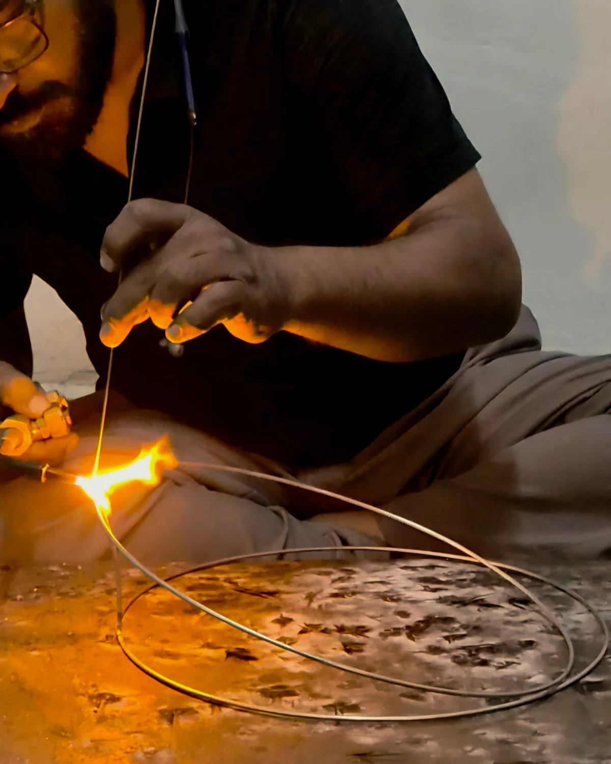 A maker joining a metal ring with a torch to form a lampshade frame.