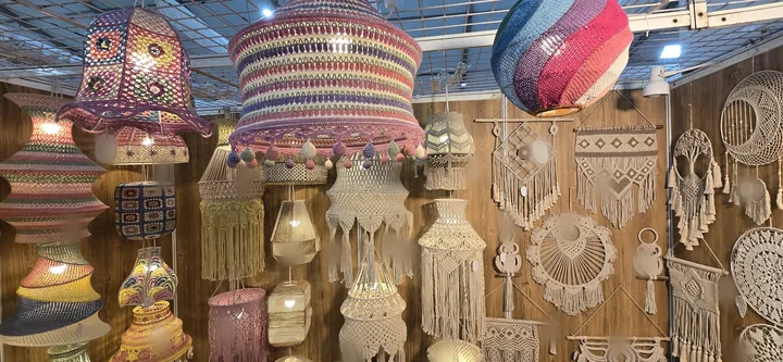 Colourful crochet pendant lamps hanging in front of a wall of cream macramé lamps and wall hangings at our stall, IHGF Delhi Fair Spring 2025.