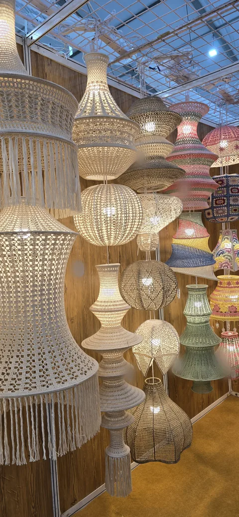 Rows of lit crochet and macramé pendant lamps in cream, grey, sage and pastel stripes hanging together at our stall, IHGF Delhi Fair Spring 2025.