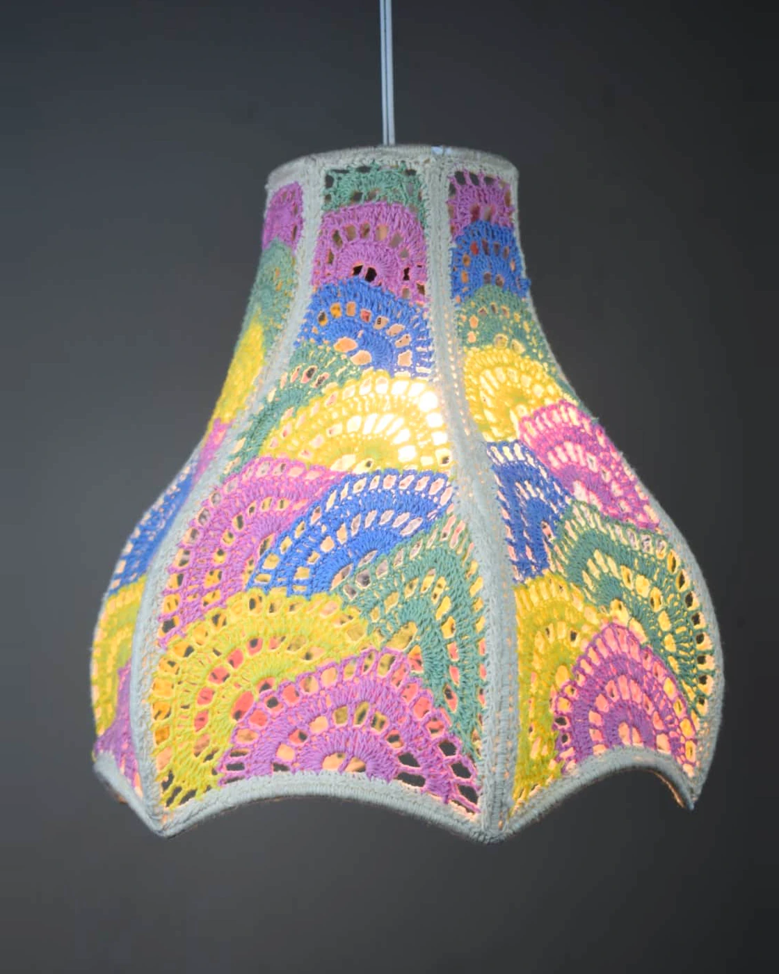 Scalloped multicolour crocheted pendant lamp shown illuminated.