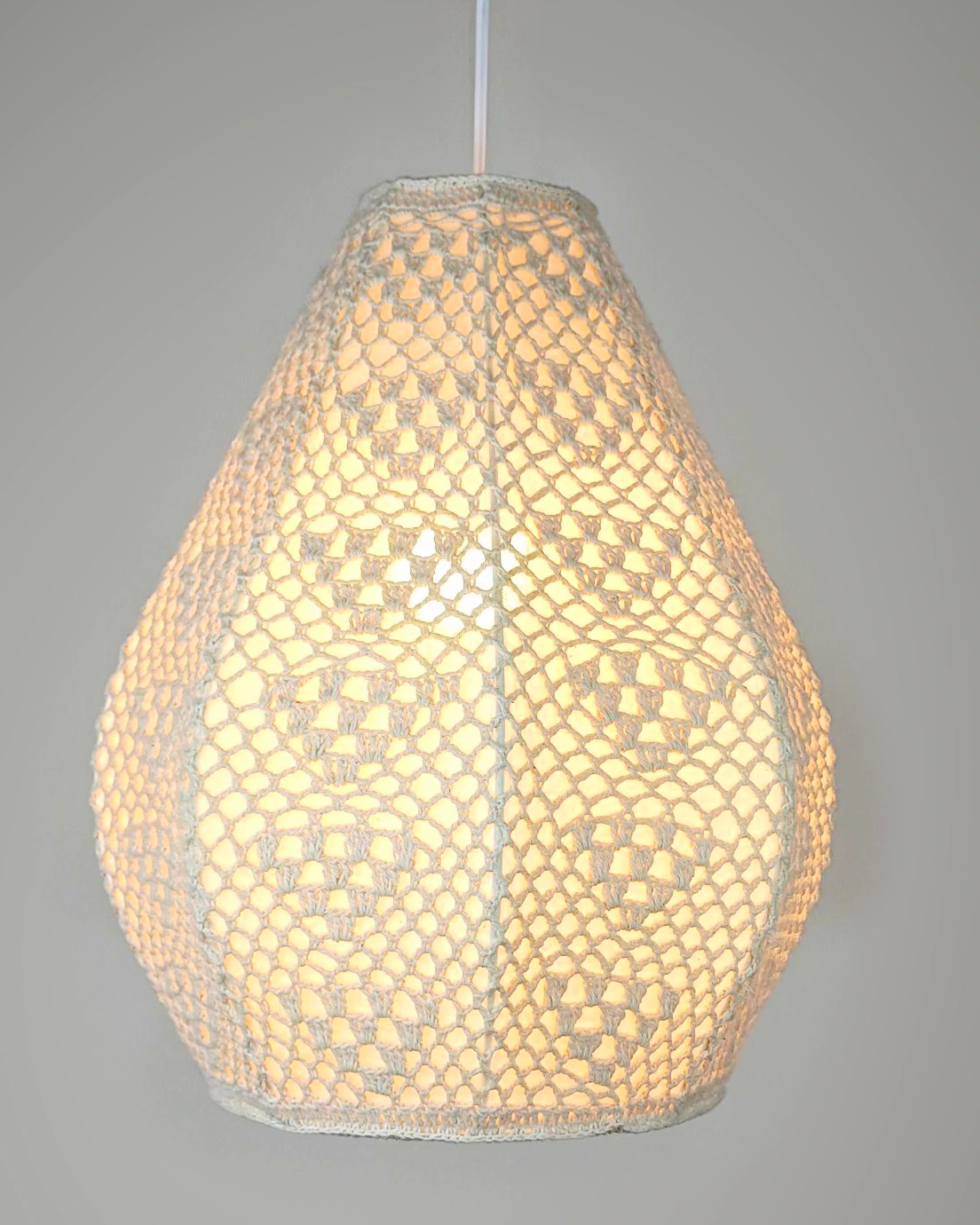 Cream crocheted teardrop pendant lamp shown illuminated.