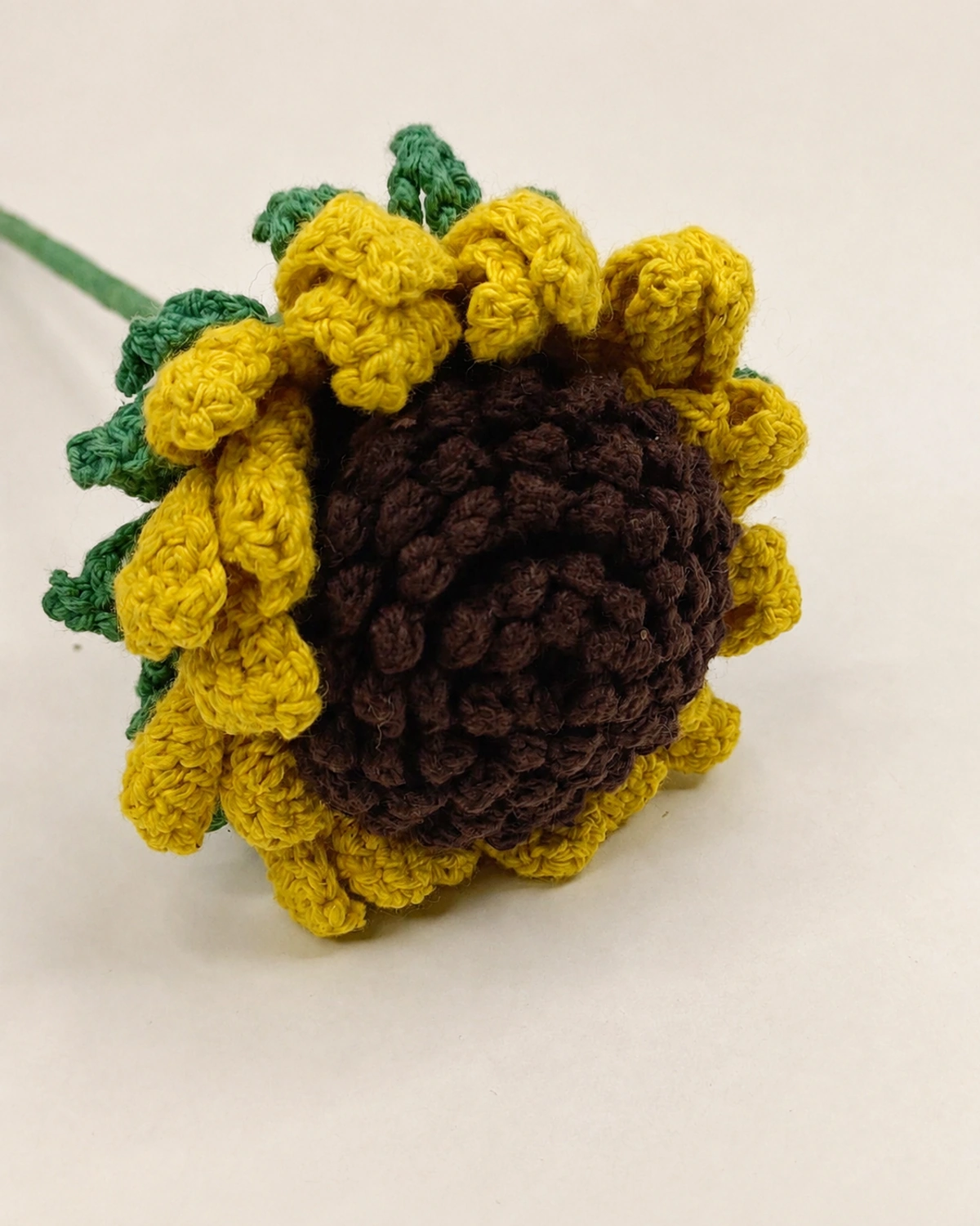 Close-up of a crochet sunflower head with yellow petals and a dark brown centre.