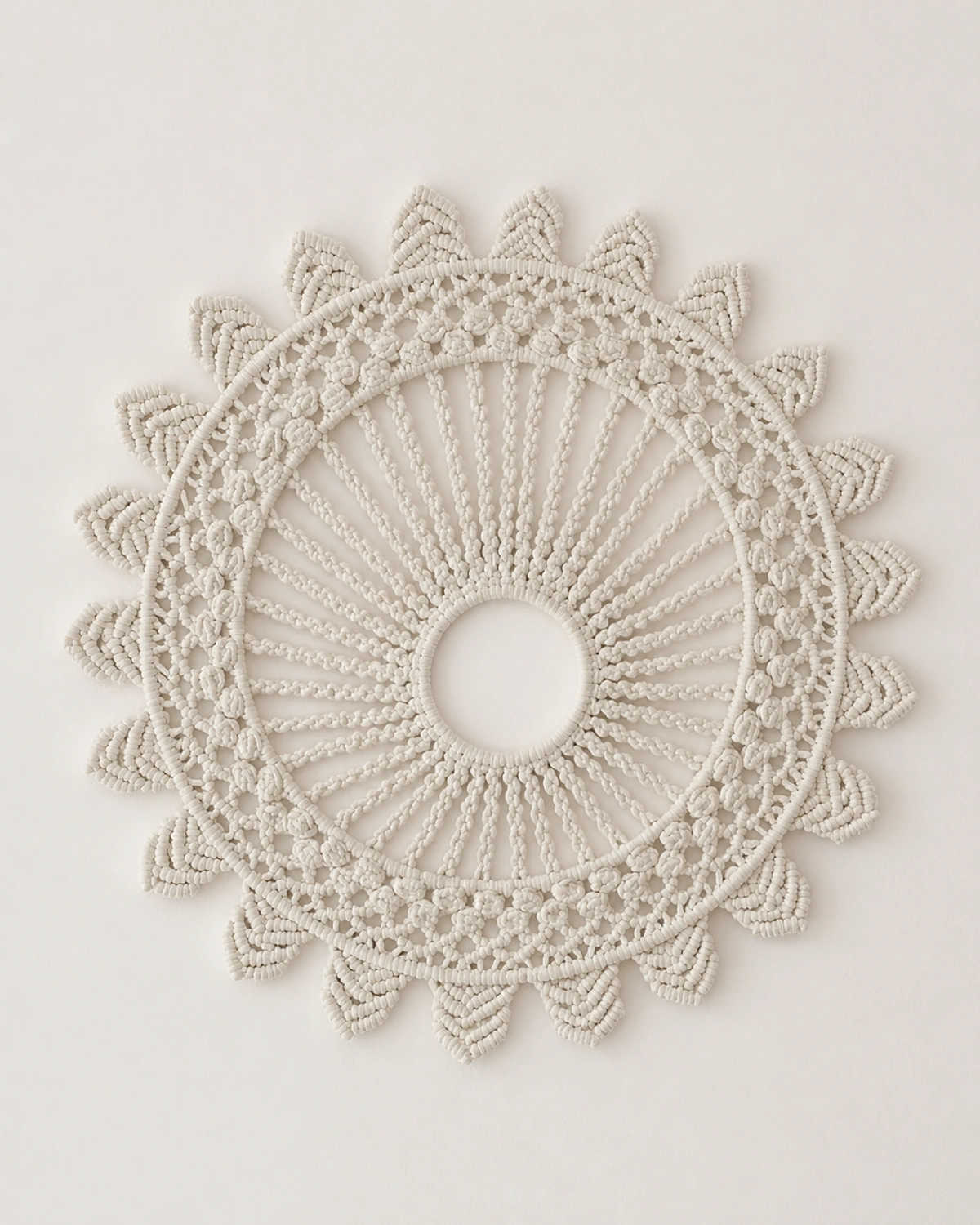 Round cream macramé wall hanging with radiating cords and leaf-shaped edging.